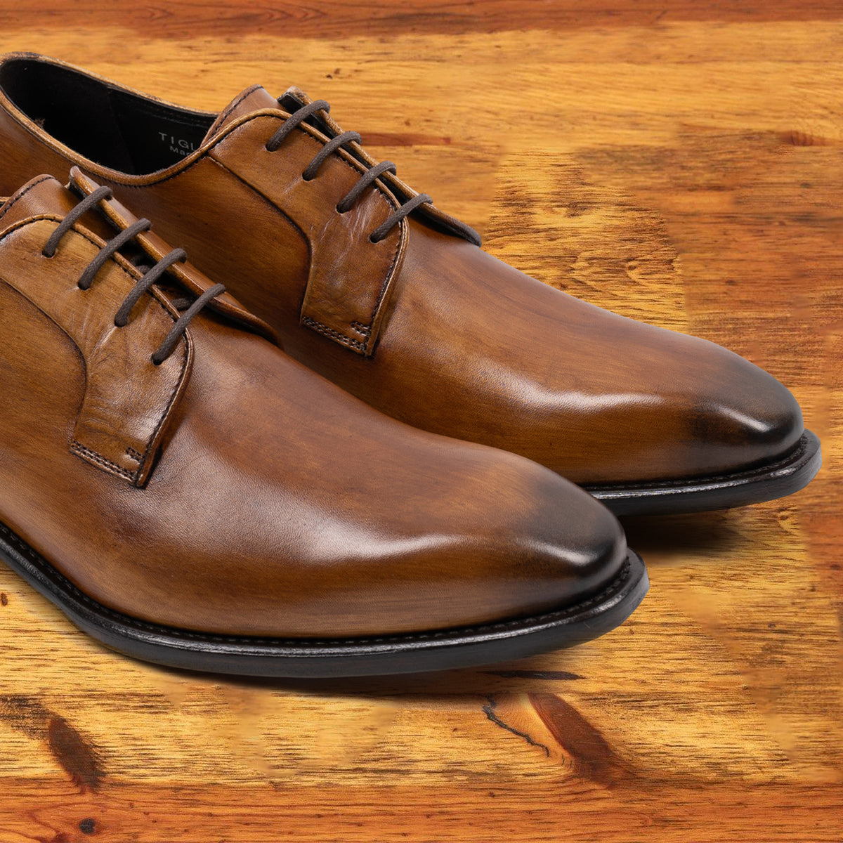 A Pair of Chestnut, wholecut blucher dress shoe with a lace-up closure, displayed on a wooden surface.