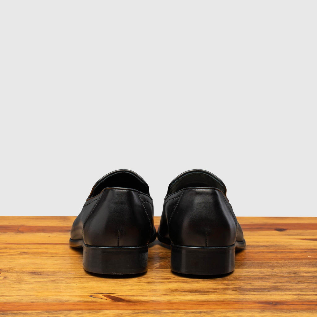 Back profile of H614 Calzoleria Toscana Black Tassel Slip-On on top of a wooden table
