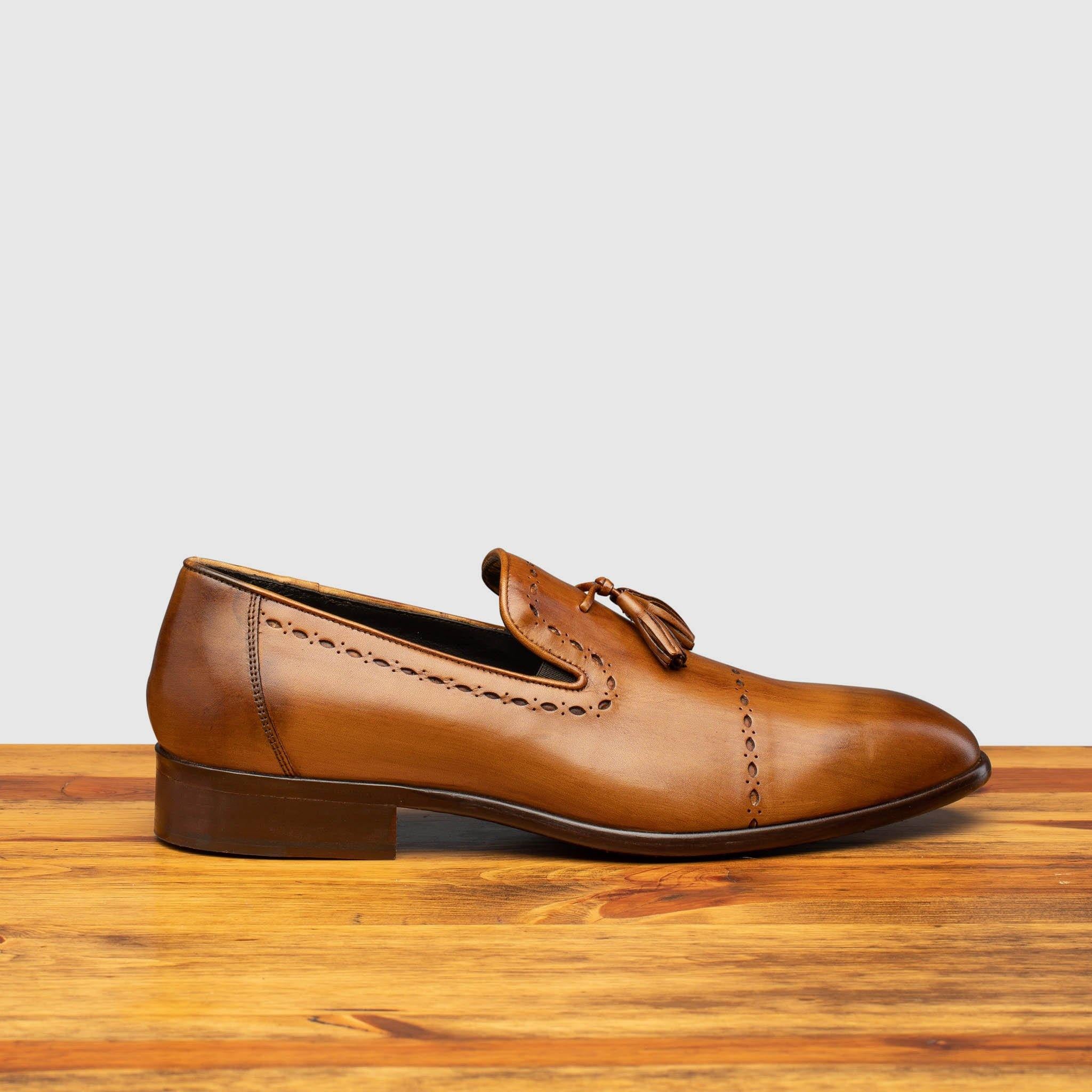 Side profile of H614 Calzoleria Toscana Chestnut Tassel Slip-On on top of a wooden table