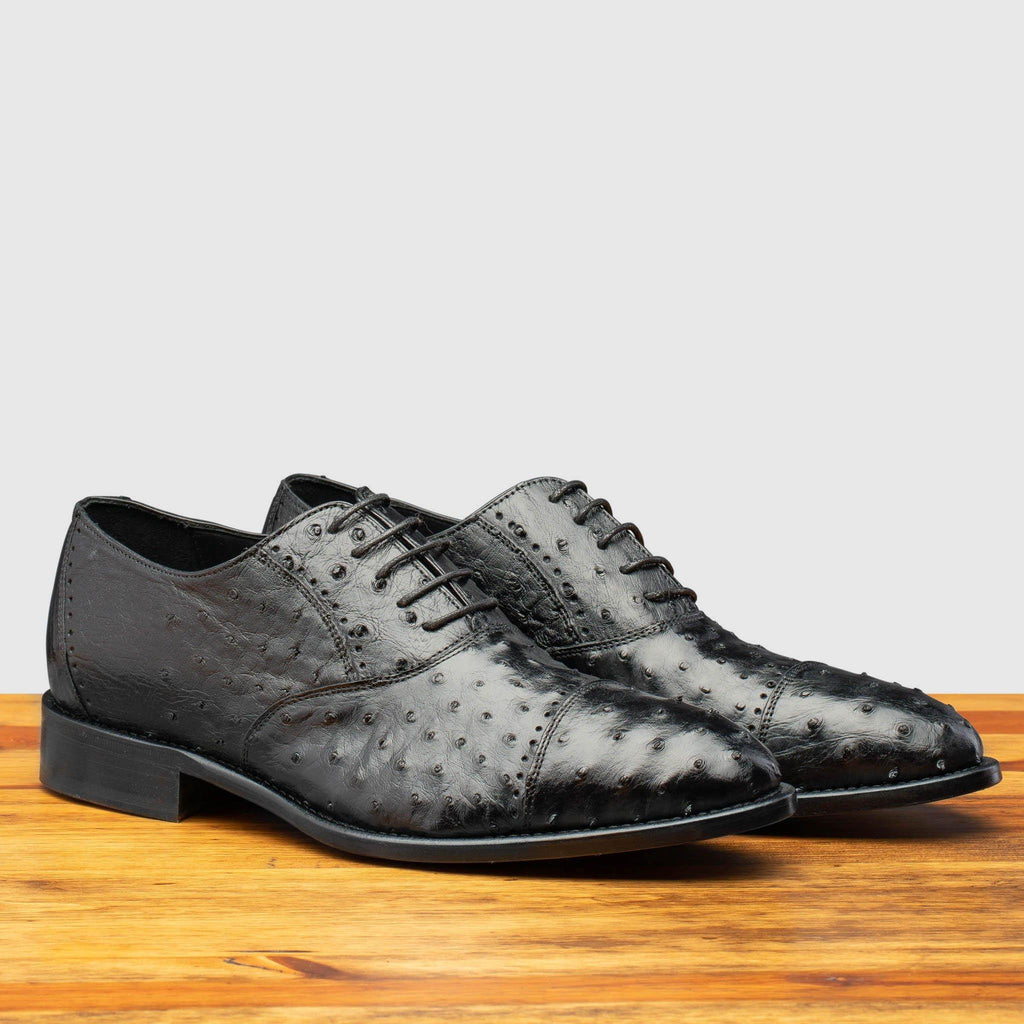 Pair of H777 Calzoleria Toscana Black Ostrich Cap Toe on top of a wooden table