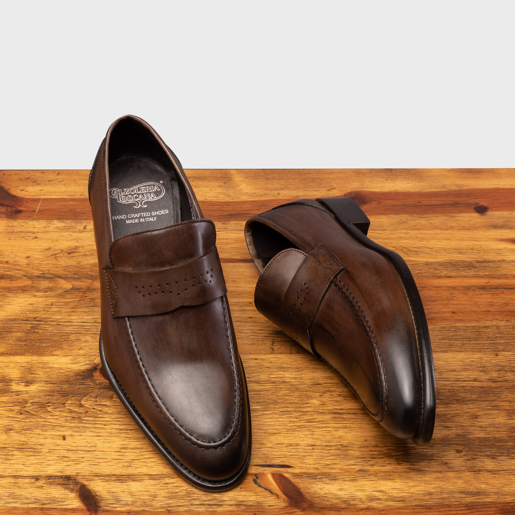 Pair of Q540 Calzoleria Toscana Moor Wholecut Slip- On showing the brand name label on top of a wooden table
