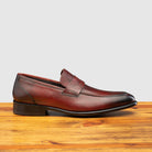 Side profile of Q540 Calzoleria Toscana Burgundy  (Porpora) Wholecut Slip-On on top of a wooden table