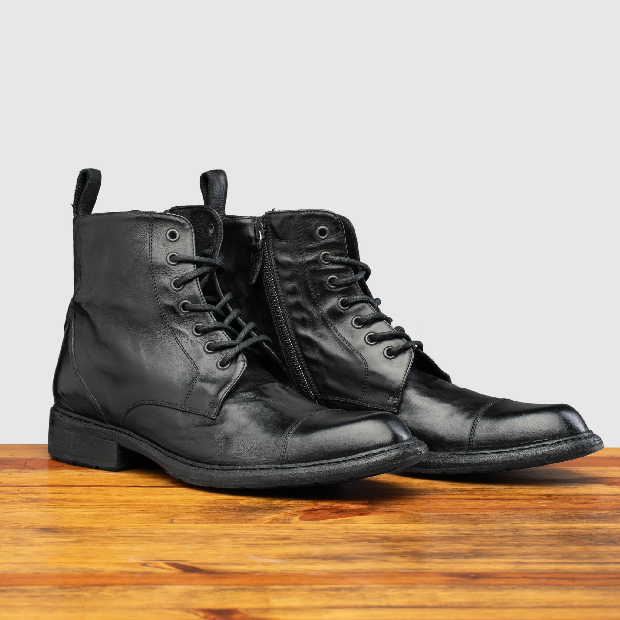 Pair of Q549 Calzoleria Toscana Black Combat Boot on top of a wooden table